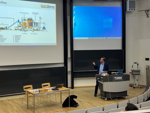 Hörsaal, unser Geschäftsführer, jr., erklärt die schematische Darstellung des Biomasseheizkraftwerkes, welche auf dem linken Großbildschirm angezeigt wird